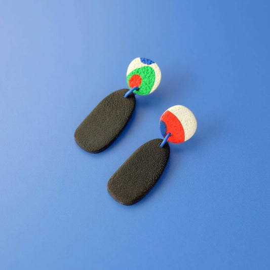 Pair of earrings with colorful circular tops and black oval bases on a blue background