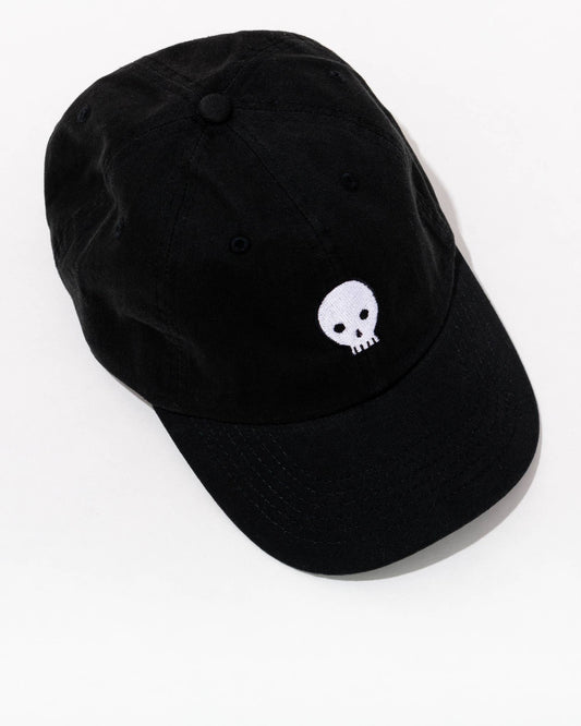 A black baseball hat made of cotton, featuring a white chain stitched skull design on the front, with an adjustable metal buckle closure.