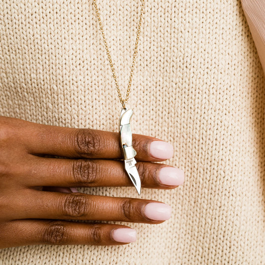 Gold necklace with a knife pendant on a hand against a beige fabric background