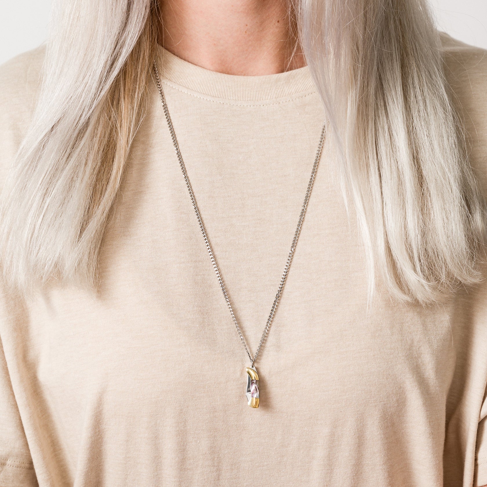 Necklace with a knife pendant worn by a person against a neutral background