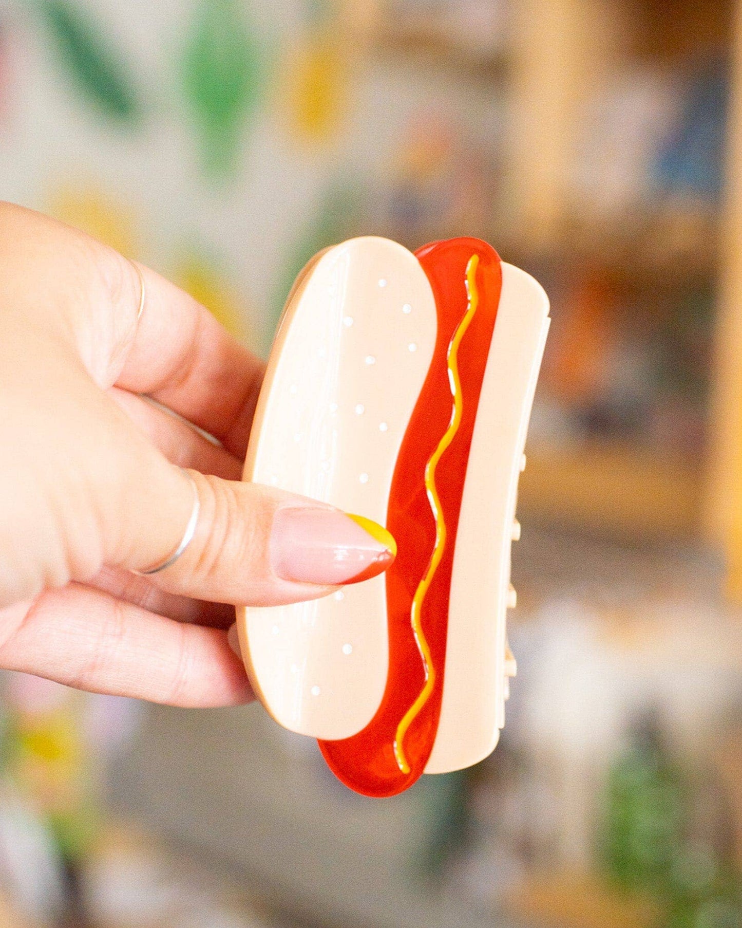 Hand holding a  hot dog hair clip against a blurred indoor background