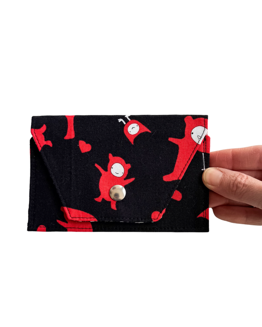 Black mini wallet pouch with red cartoon characters held by a hand on a white background