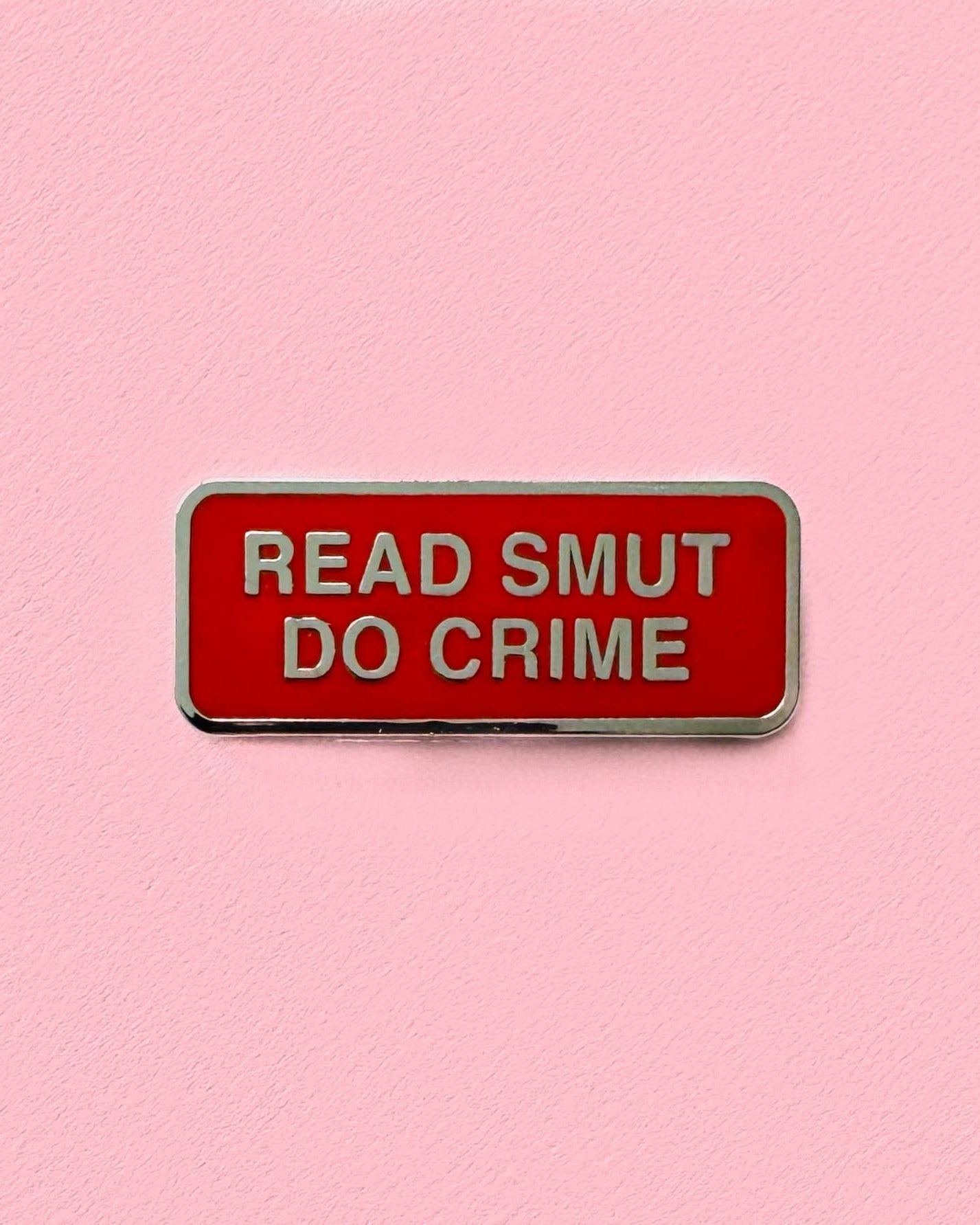 Red enamel pin with 'READ SMUT DO CRIME' text on a pink background