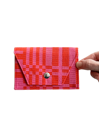 Hand holding a red and pink checkered wallet against a white background