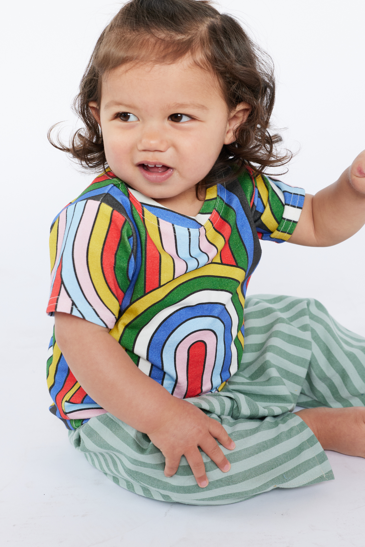 Child wearing a colorful organic cotton striped shirt and green pants on a white background