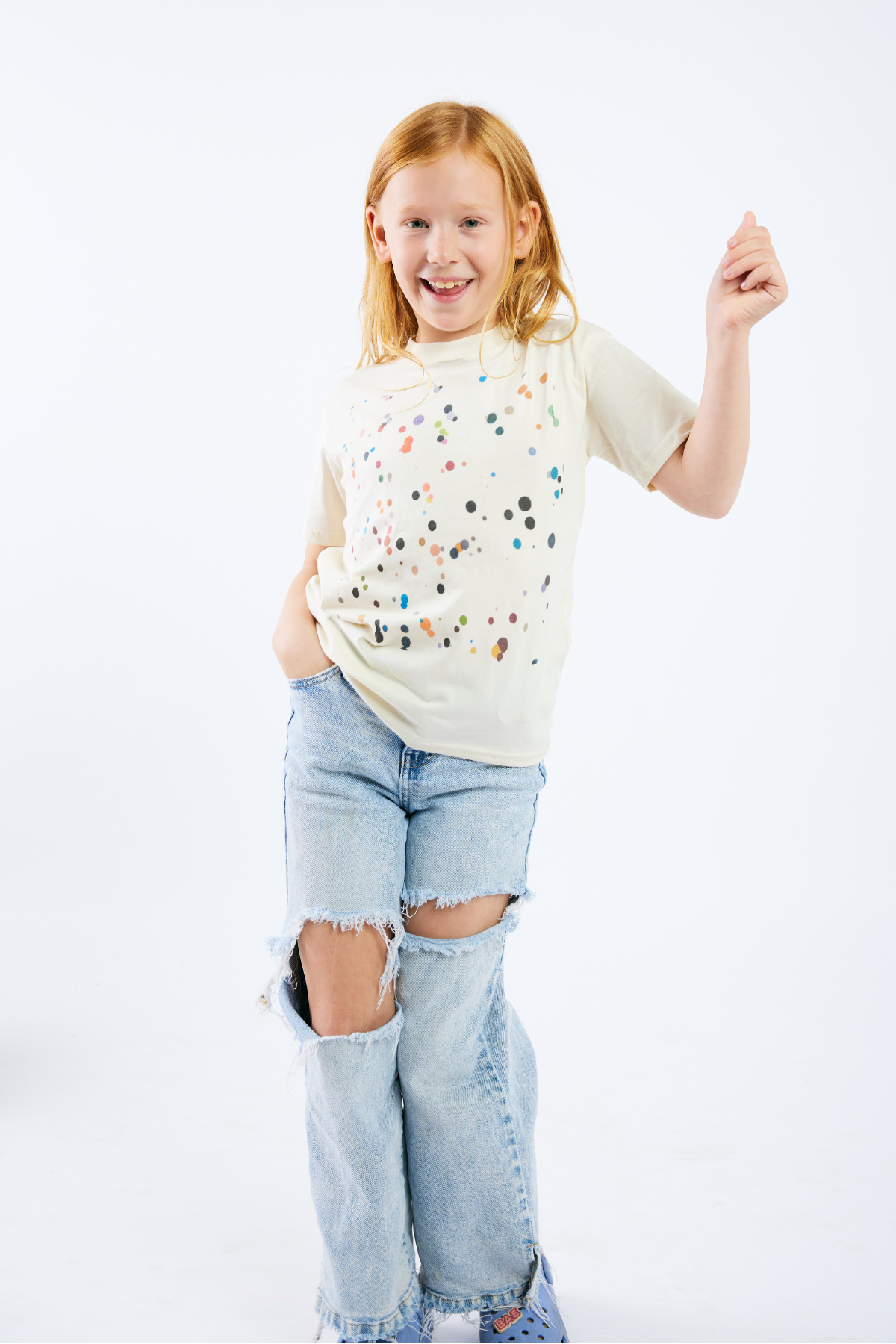 Young girl wearing a white t-shirt with colorful dots and ripped jeans on a white background