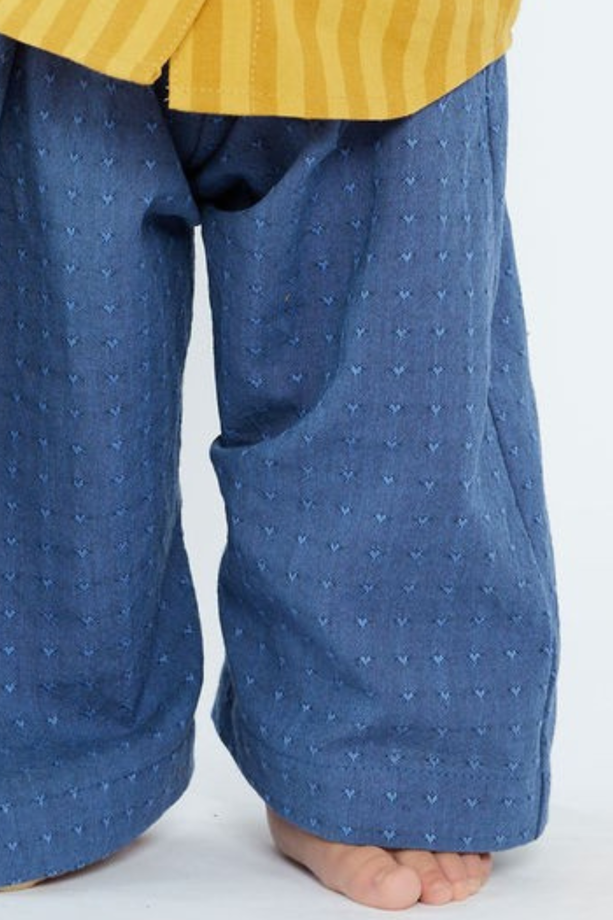 Close-up of blue pants with a subtle heart pattern worn by a child on a white background