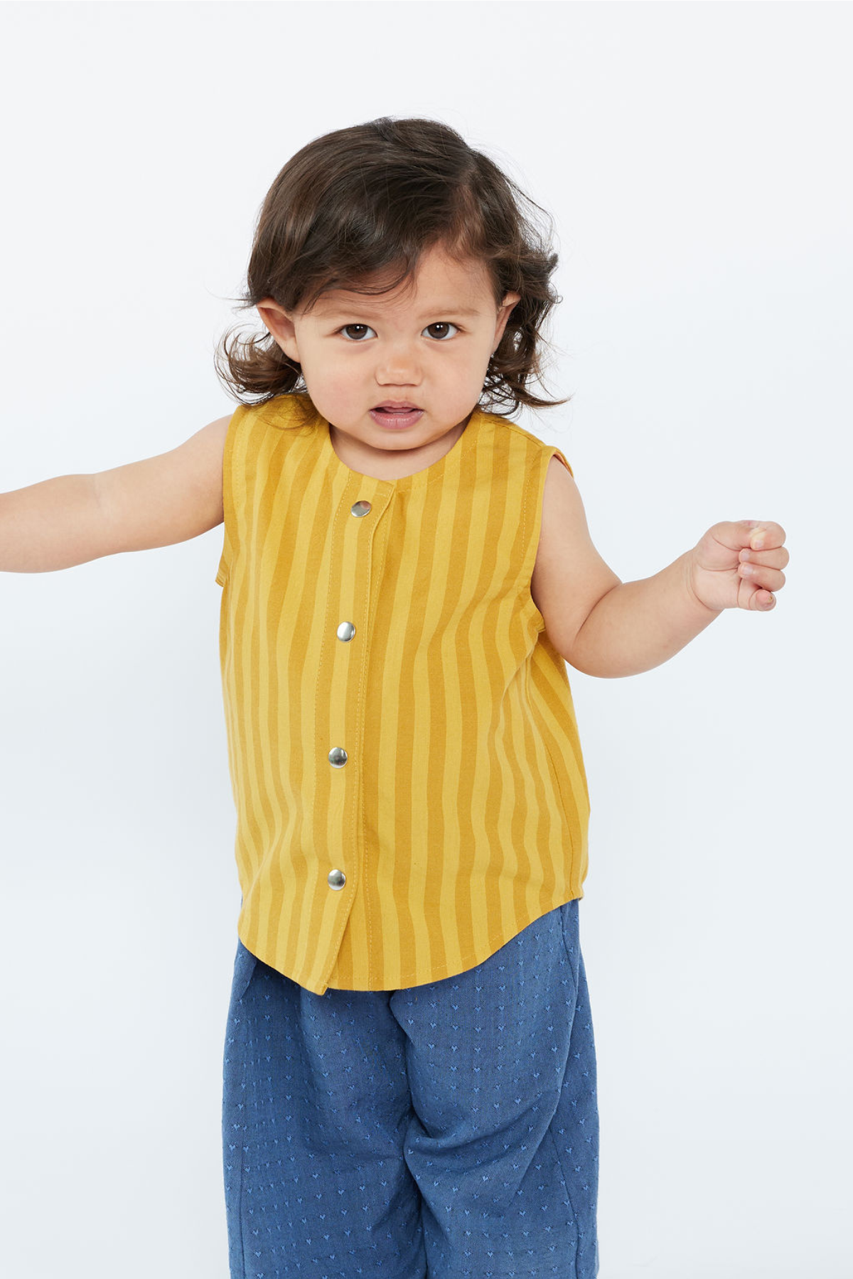 Child wearing a yellow sleeveless shirt with snaps and blue pants on a white background