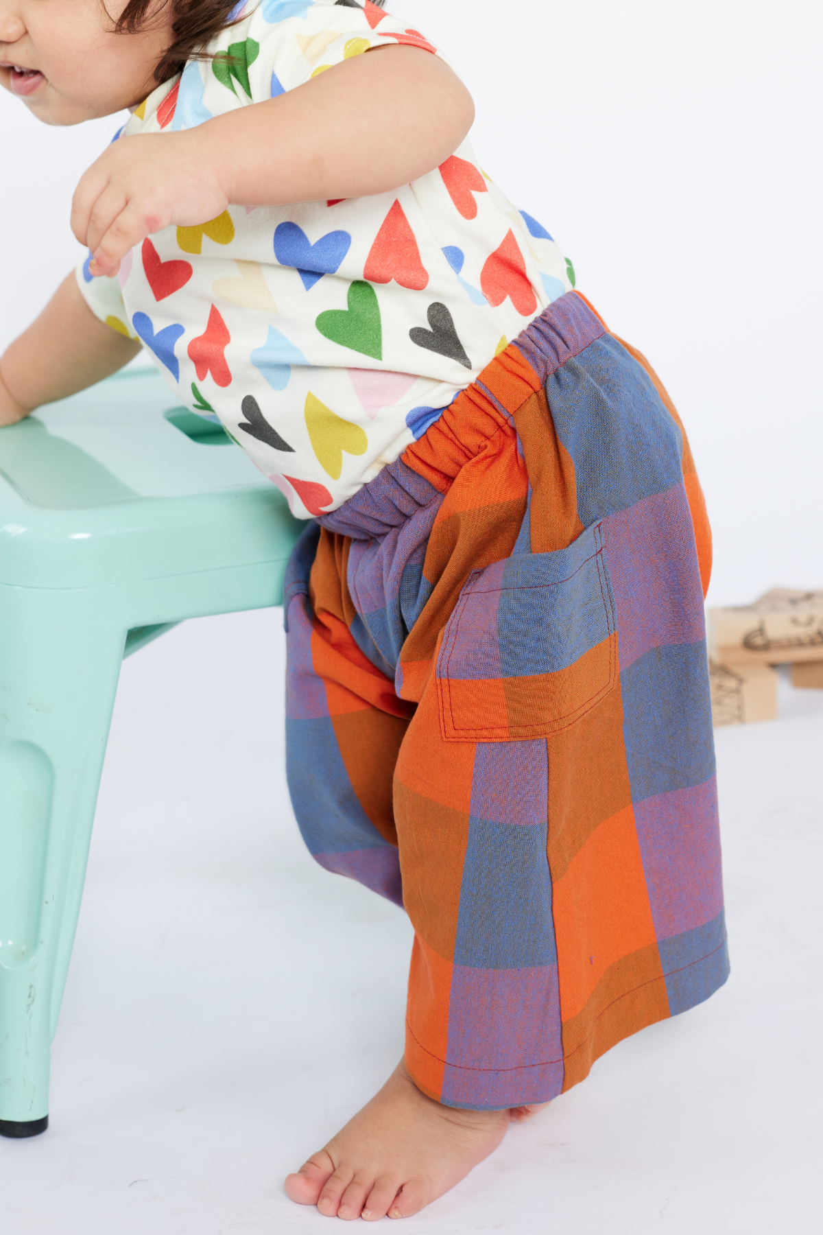 Child wearing a colorful shirt with heart patterns and red plaid pants by Lilla Barn Clothing on a white background