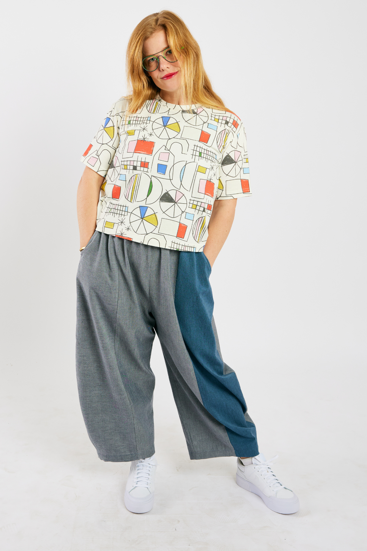 person wearing gray and blue barrel-leg pants  (with pockets) made from sustainable bamboo and cotton. She's also wearing a colorful, organic cotton t-shirt, and glasses from Eye Spy Optical.