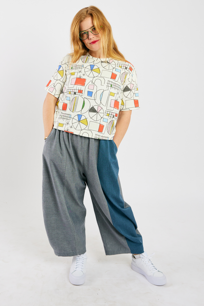 person wearing gray and blue barrel-leg pants  (with pockets) made from sustainable bamboo and cotton. She's also wearing a colorful, organic cotton t-shirt, and glasses from Eye Spy Optical.