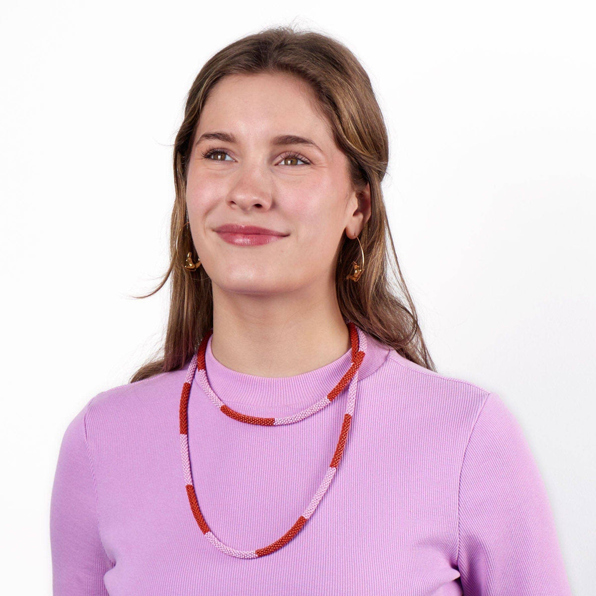 Woman wearing a pink sweater and red beaded necklace on a white background