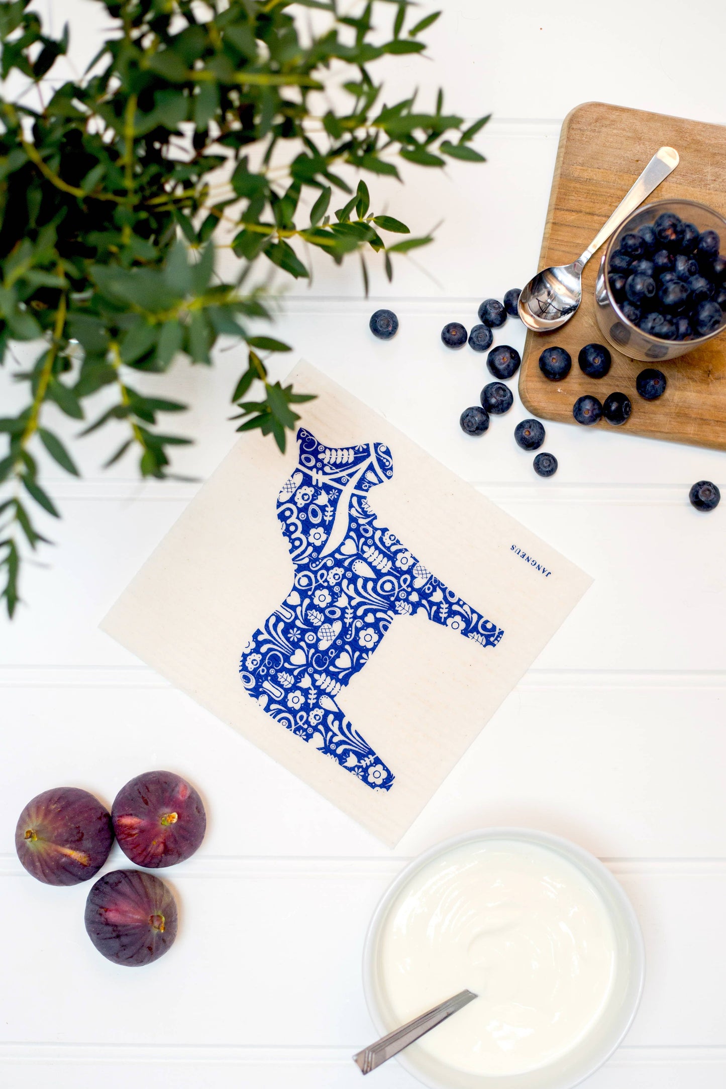 Tea towel with blue dala horse design on a white surface with fruits and a plant.