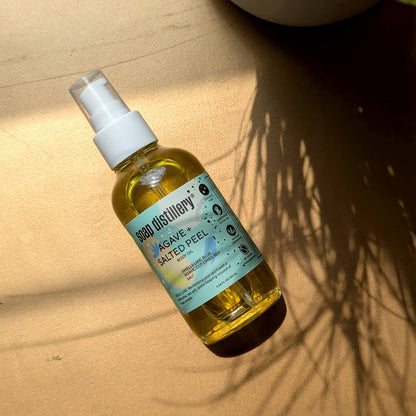 Bottle of 'Agave + Salted Peel' body oil from Soap Distillery on a sandy background