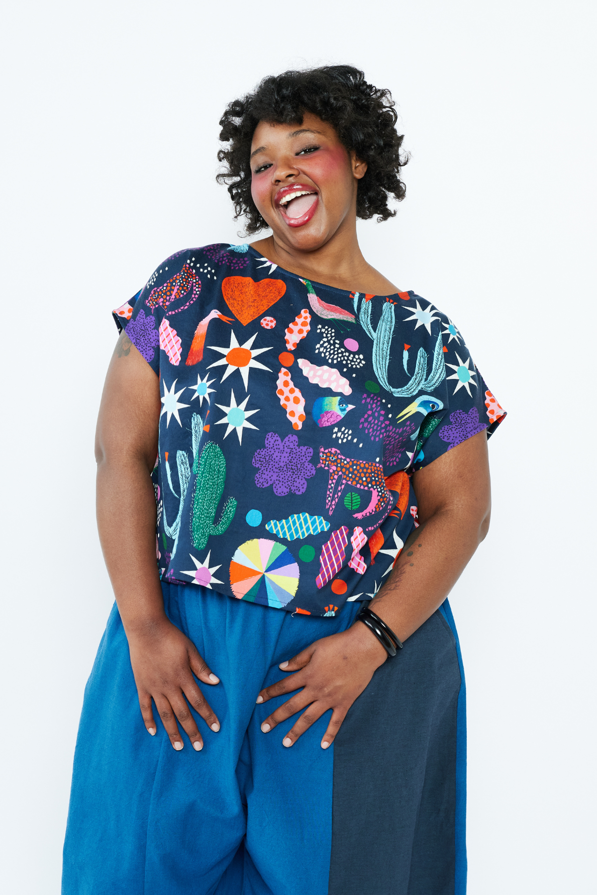 Person wearing a colorful patterned top and blue pants on a white background