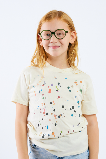 Young girl wearing a cream t-shirt with colorful polka dots and glasses on a white background