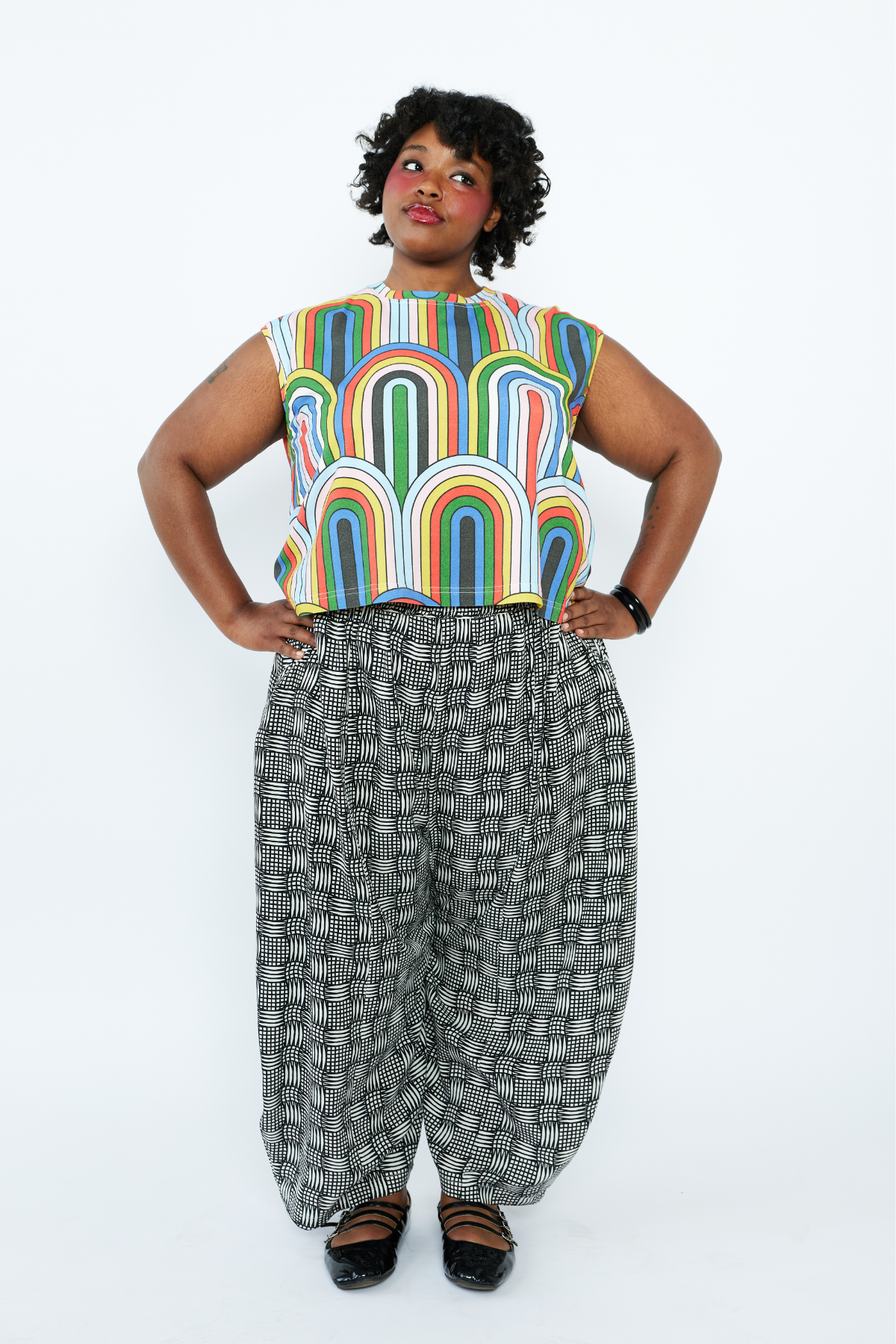 Person wearing a colorful sleeveless top and patterned pants on a white background