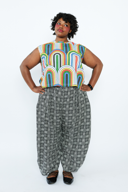Person wearing a colorful sleeveless top and patterned pants on a white background
