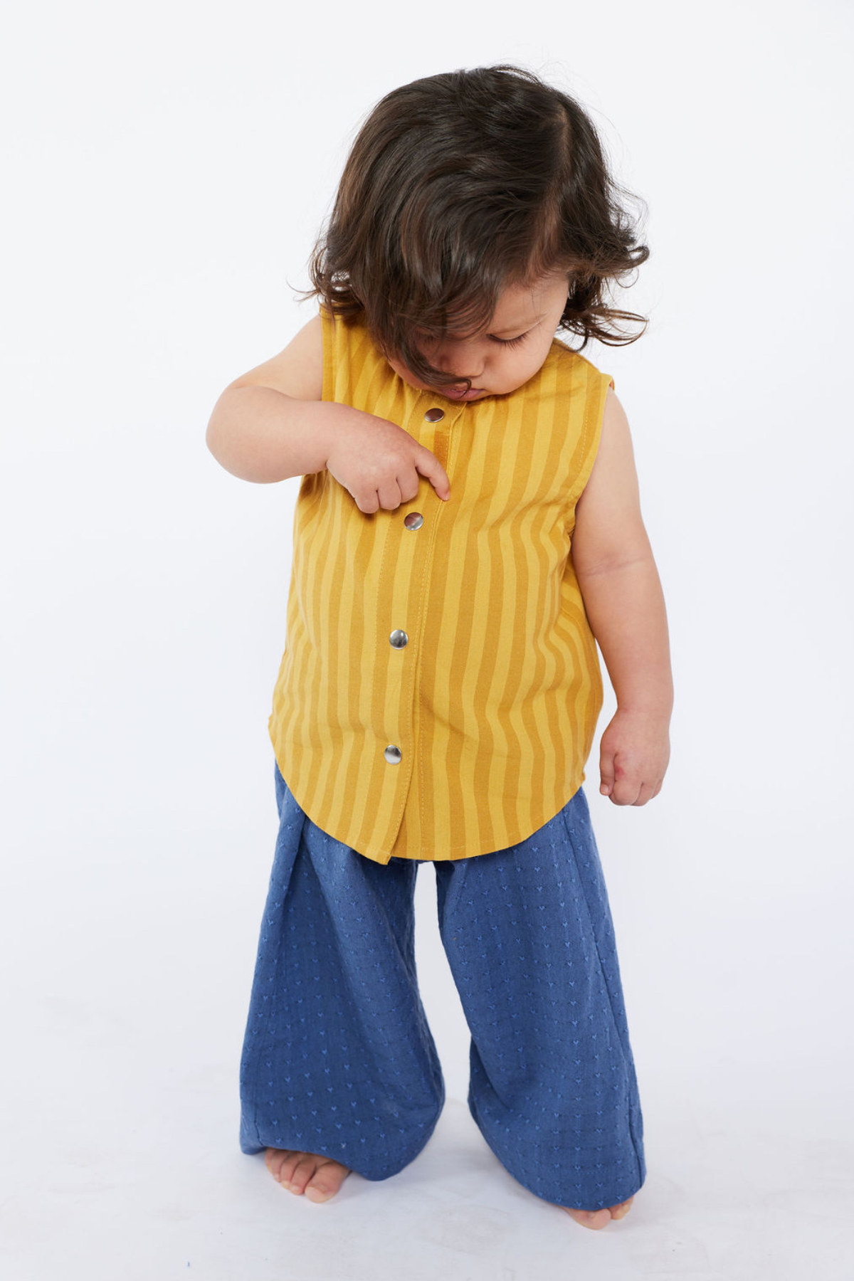 Child wearing a yellow striped shirt and blue pants on a white background