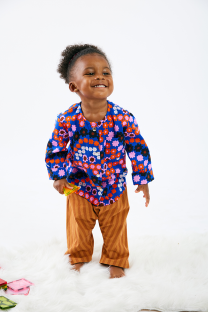 Child smiling and wearing a colorful floral shirt and brown pants on a white background