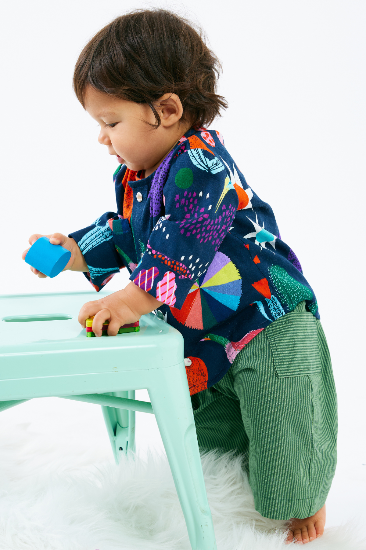 Child wearing a colorful baby clothes with a pattern of animals and plants on a white background