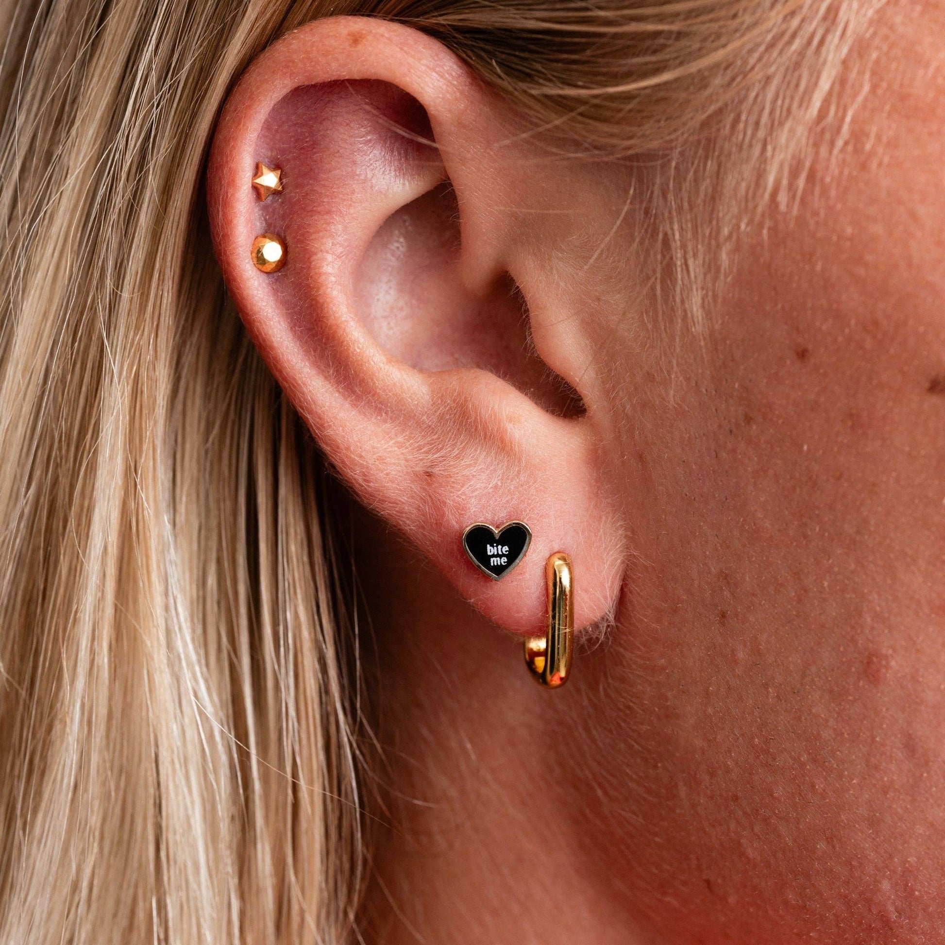 Close-up of an ear with multiple earrings including a heart-shaped one.