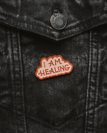 enamel pin with 'I AM HEALING' text on a black denim jacket