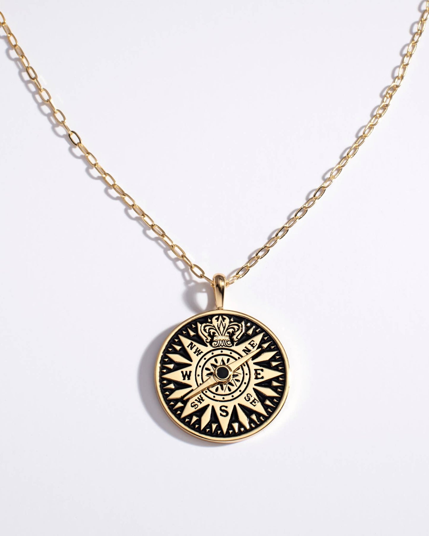 Gold necklace with a black compass pendant on a white background