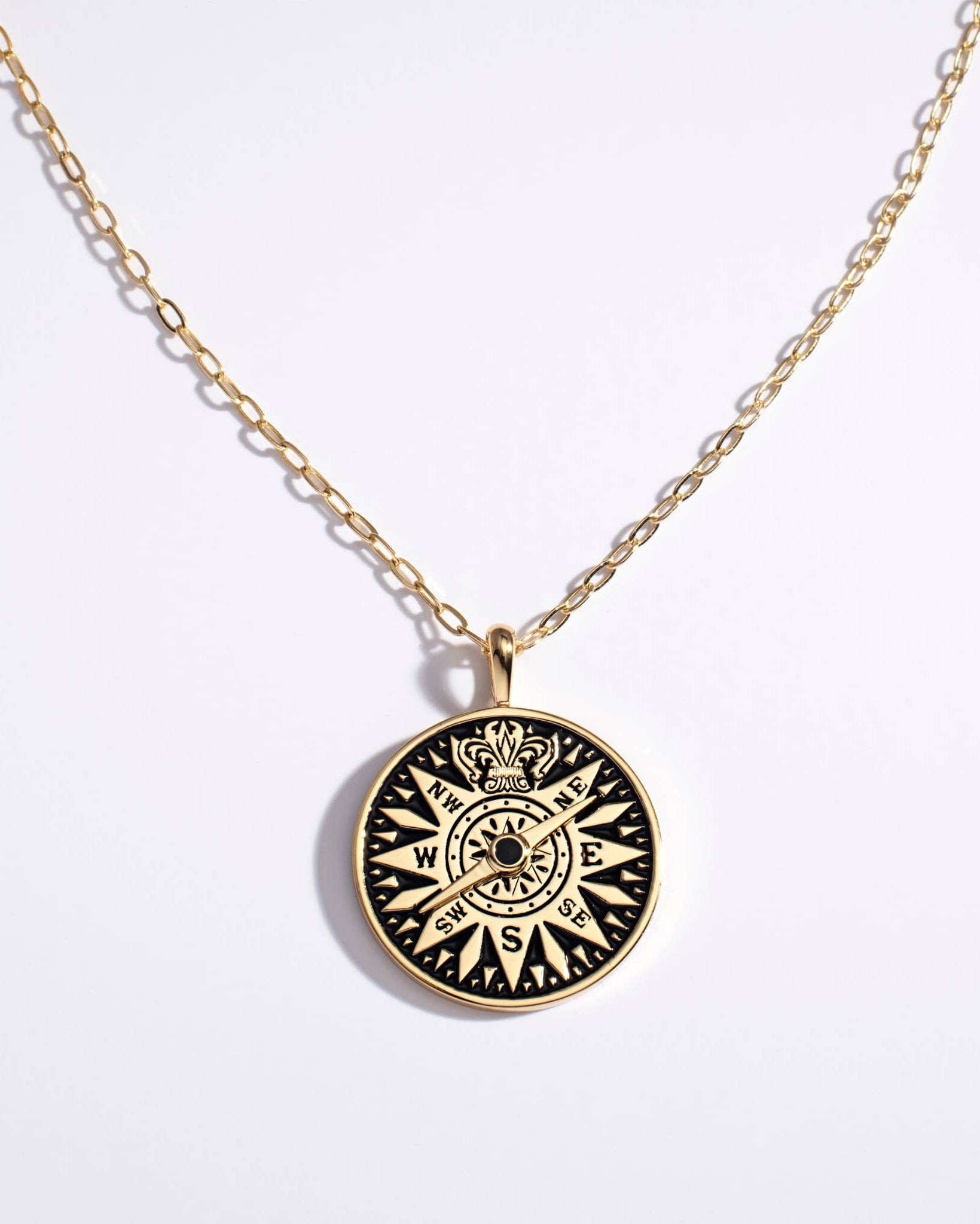 Gold necklace with a black compass pendant on a white background
