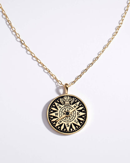 Gold necklace with a black compass pendant on a white background