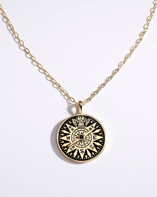 Gold necklace with a black compass pendant on a white background