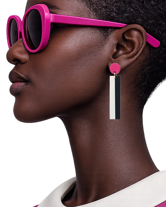 A close-up side profile of a model wearing bright pink sunglasses and a matching pink earring with a vertical black-and-white rectangular drop, against a clean white background.