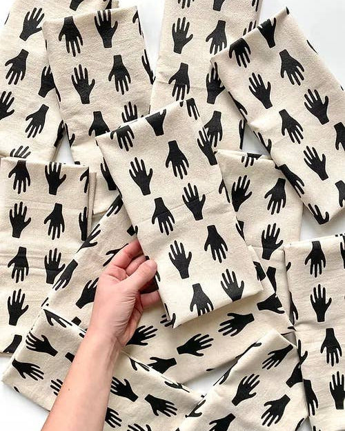 cotton tea towel with black hand pattern held by a hand against a white background