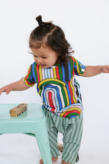 Child wearing a colorful striped shirt and green striped pants, standing next to a light blue table.