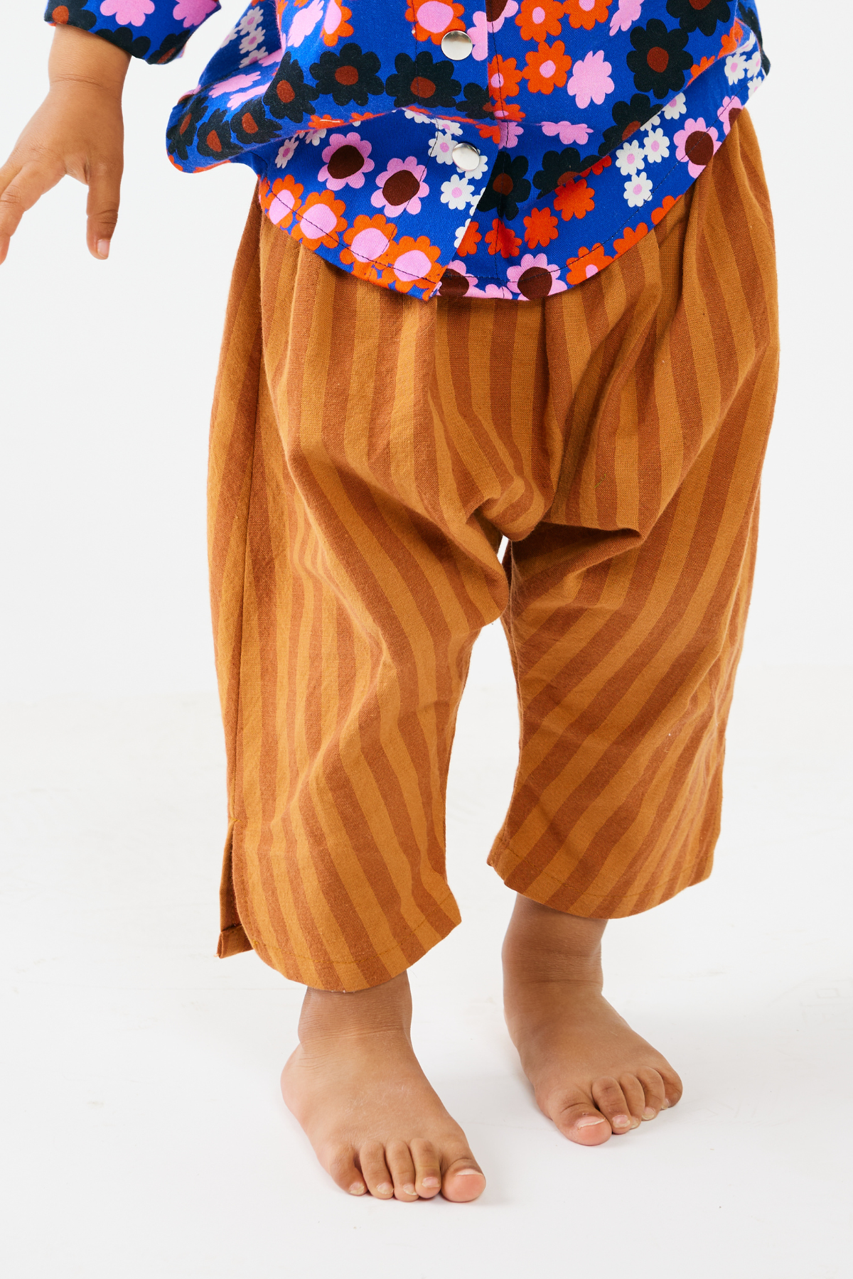child wearing a colorful floral top and brown striped pants on a white background