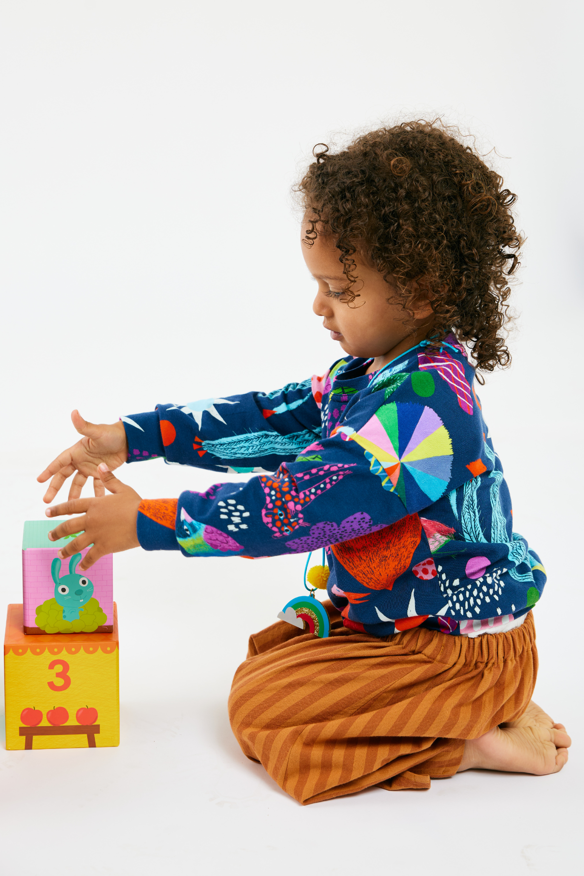 Child playing with blocks and wearing a colorful kid top and striped pants by Lilla Barn Clothing