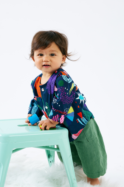 Child wearing a colorful baby clothes with a pattern of animals and plants on a white background