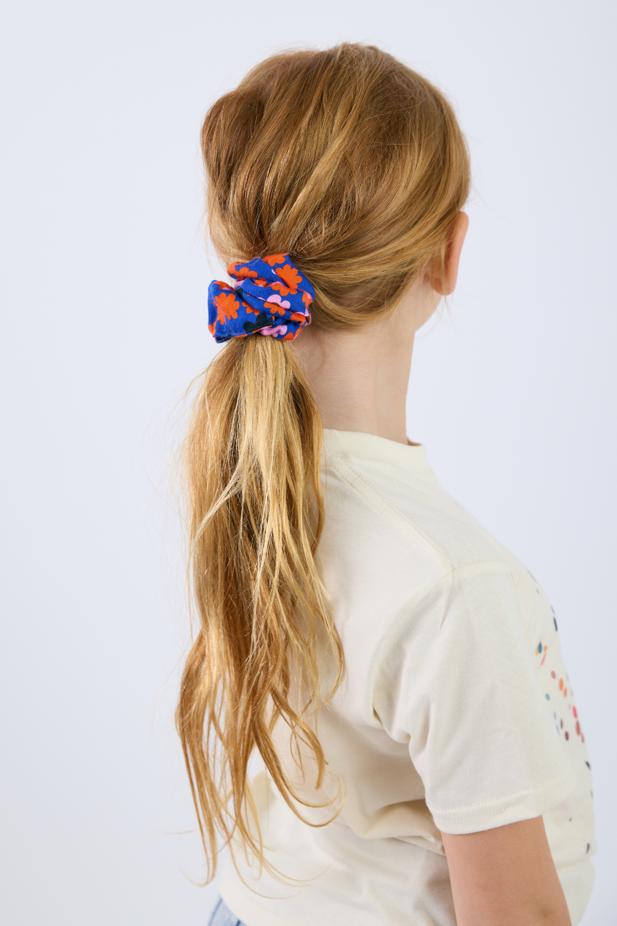 Person with a ponytail held by a colorful scrunchie on a white background