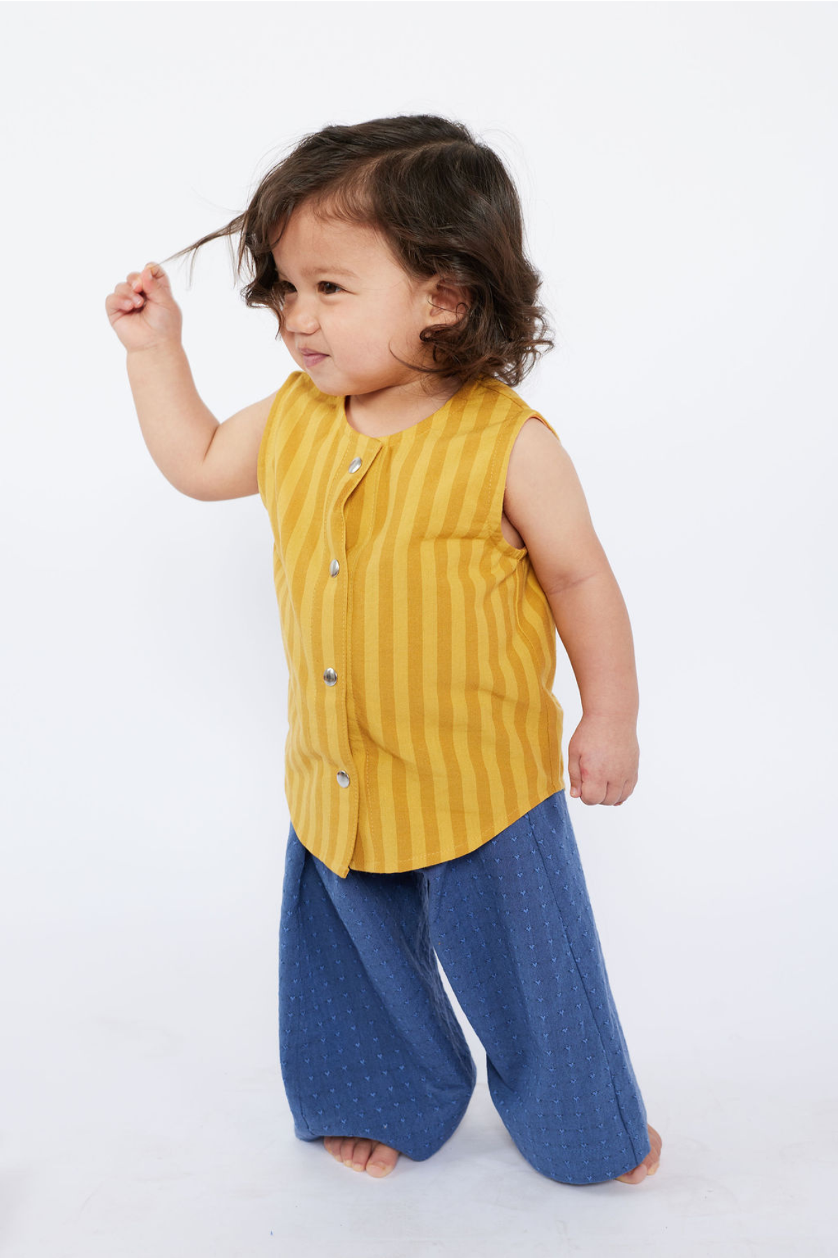 Child wearing a yellow sleeveless shirt and blue pants on a white background
