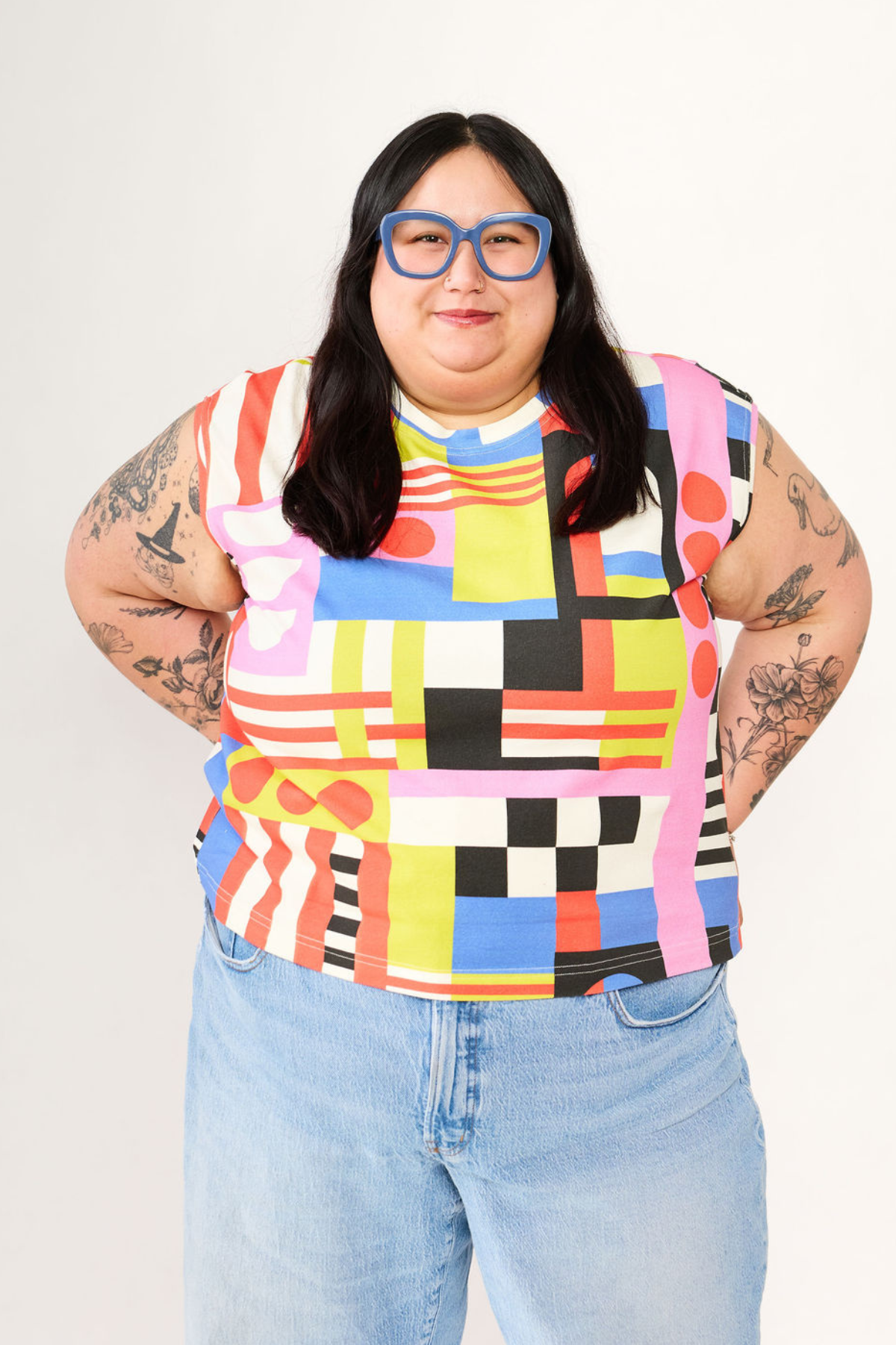 Person wearing a colorful geometric-patterned sleeveless top and light blue jeans on a white background