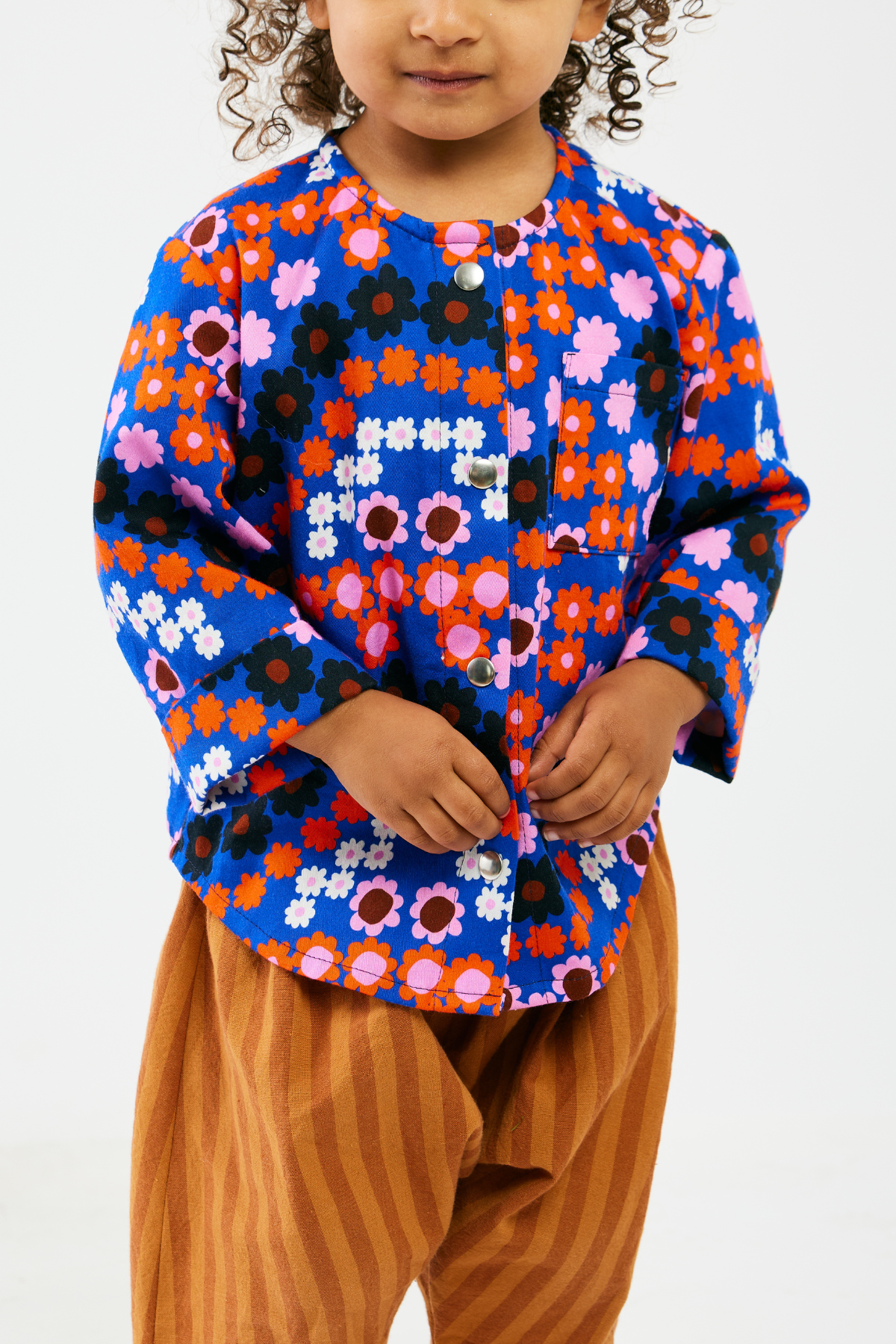 Child wearing a colorful floral-patterned shirt with brown stripe pants on a white background