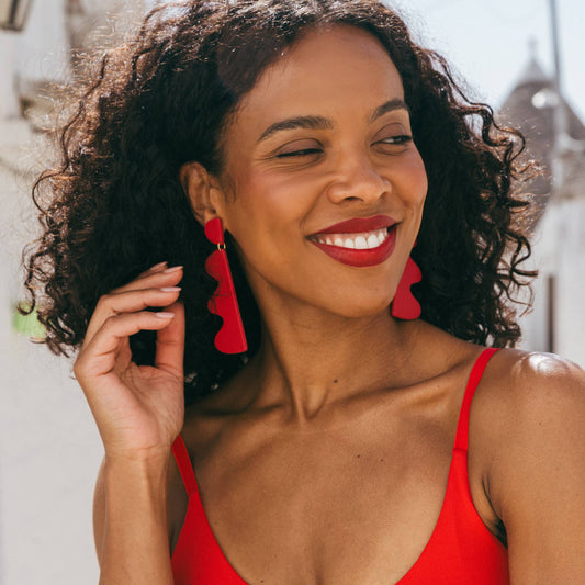 Woman wearing red earrings and a red top, smiling outdoors.