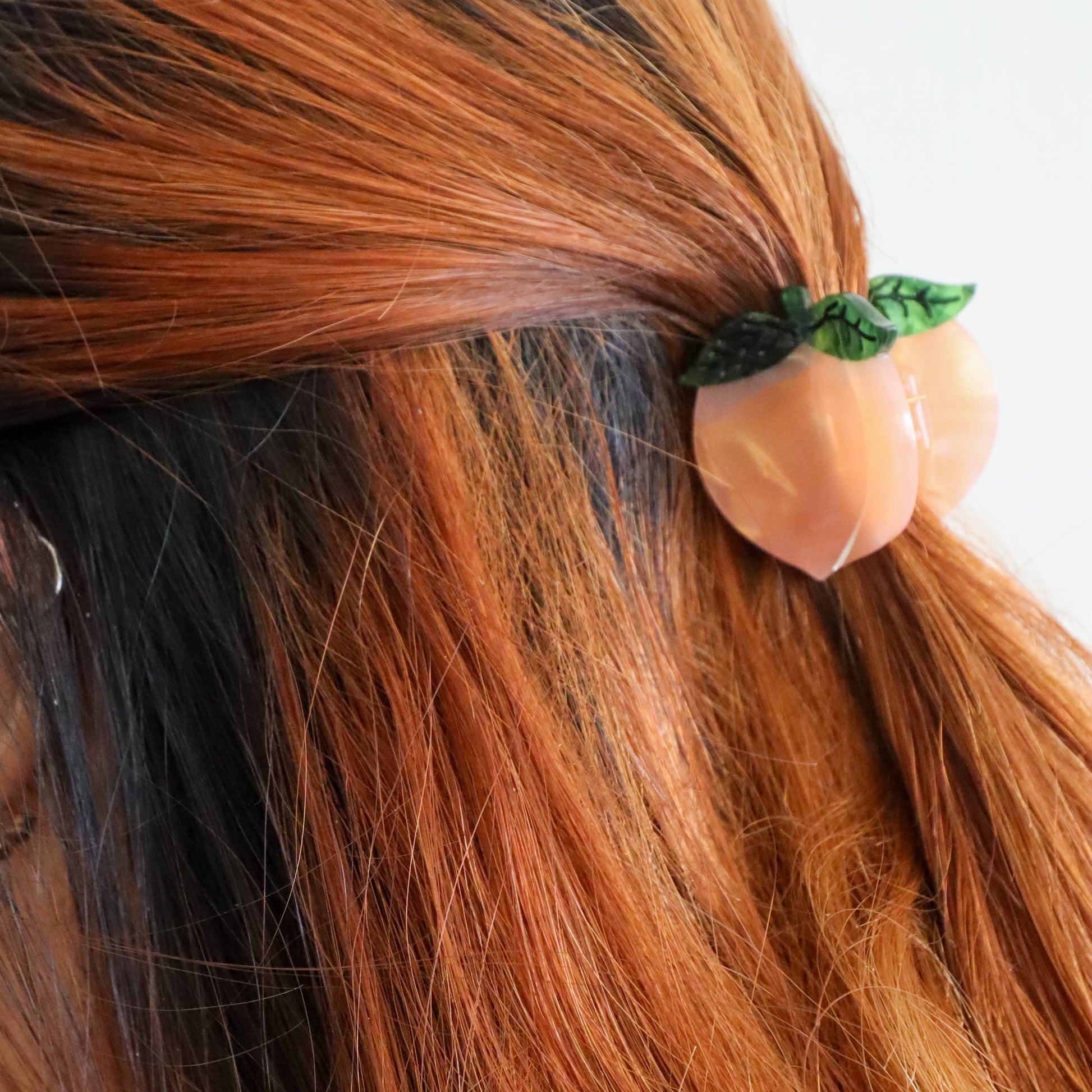 Hair clip shaped like a peach with green leaves in brown hair