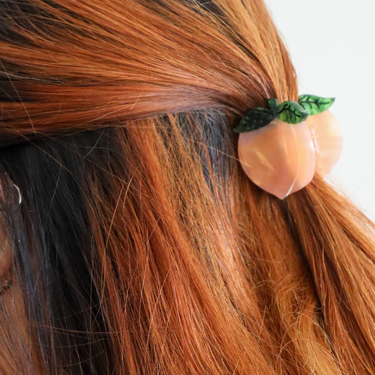 Hair clip shaped like a peach with green leaves in brown hair