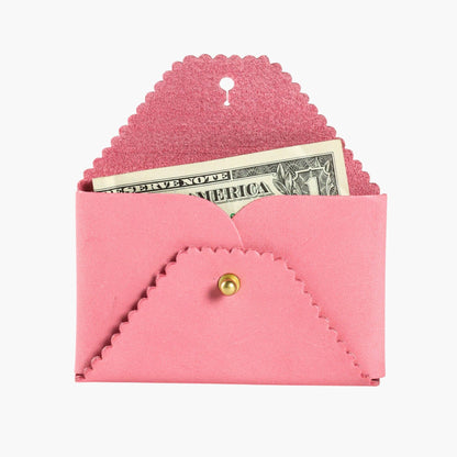 Pink envelope-shaped wallet with scalloped edges and a gold button, containing a dollar bill on a white background.