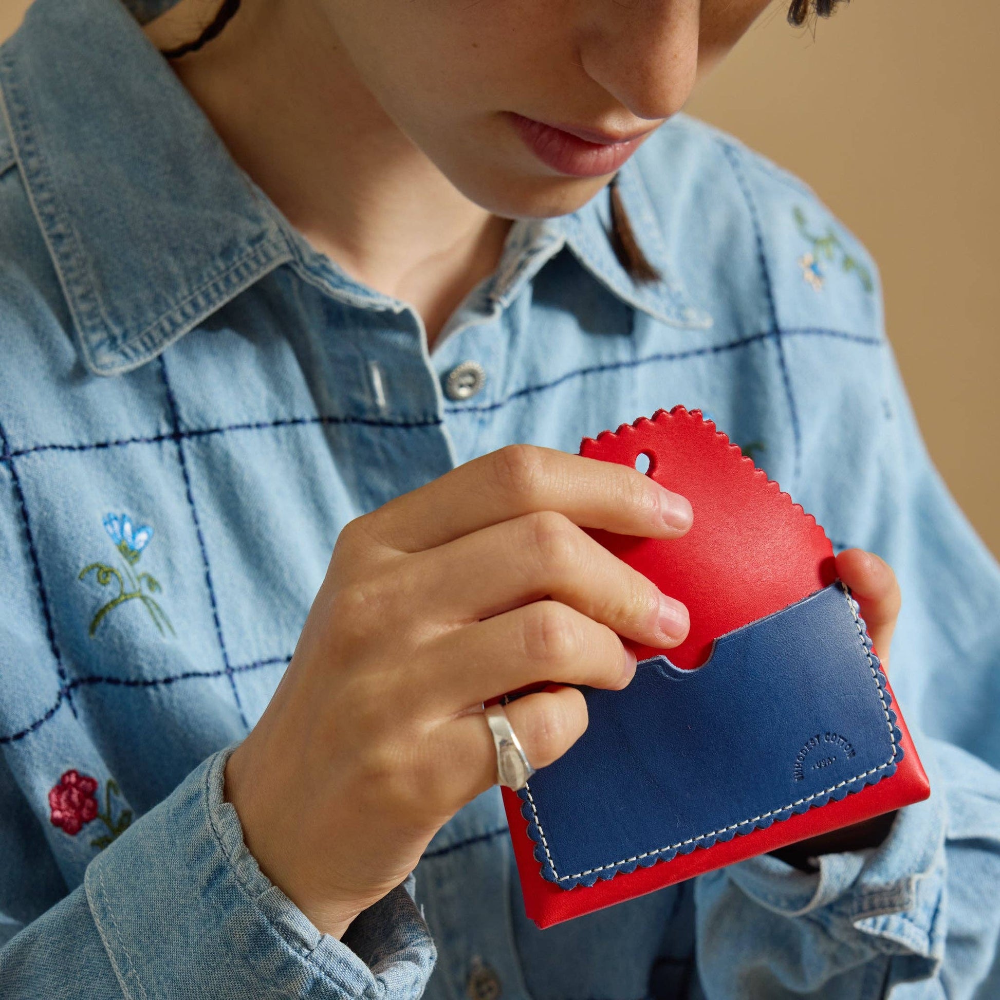 Person holding a red and blue wallet with a denim jacket