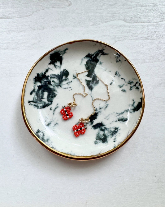 woven beaded butterfly ear threaders in red beads sitting in a marbled stone bowl
