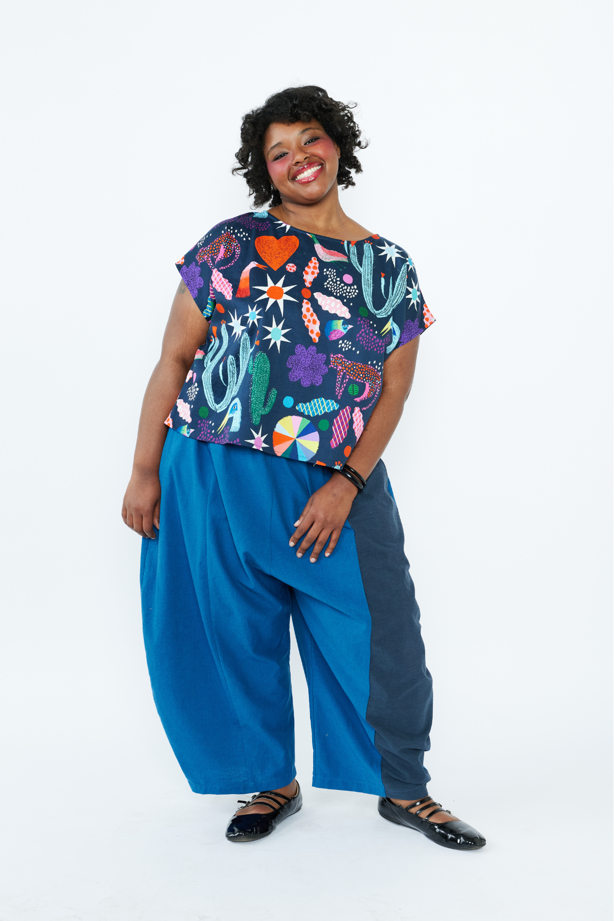 Person wearing a colorful patterned top and blue pants on a white background