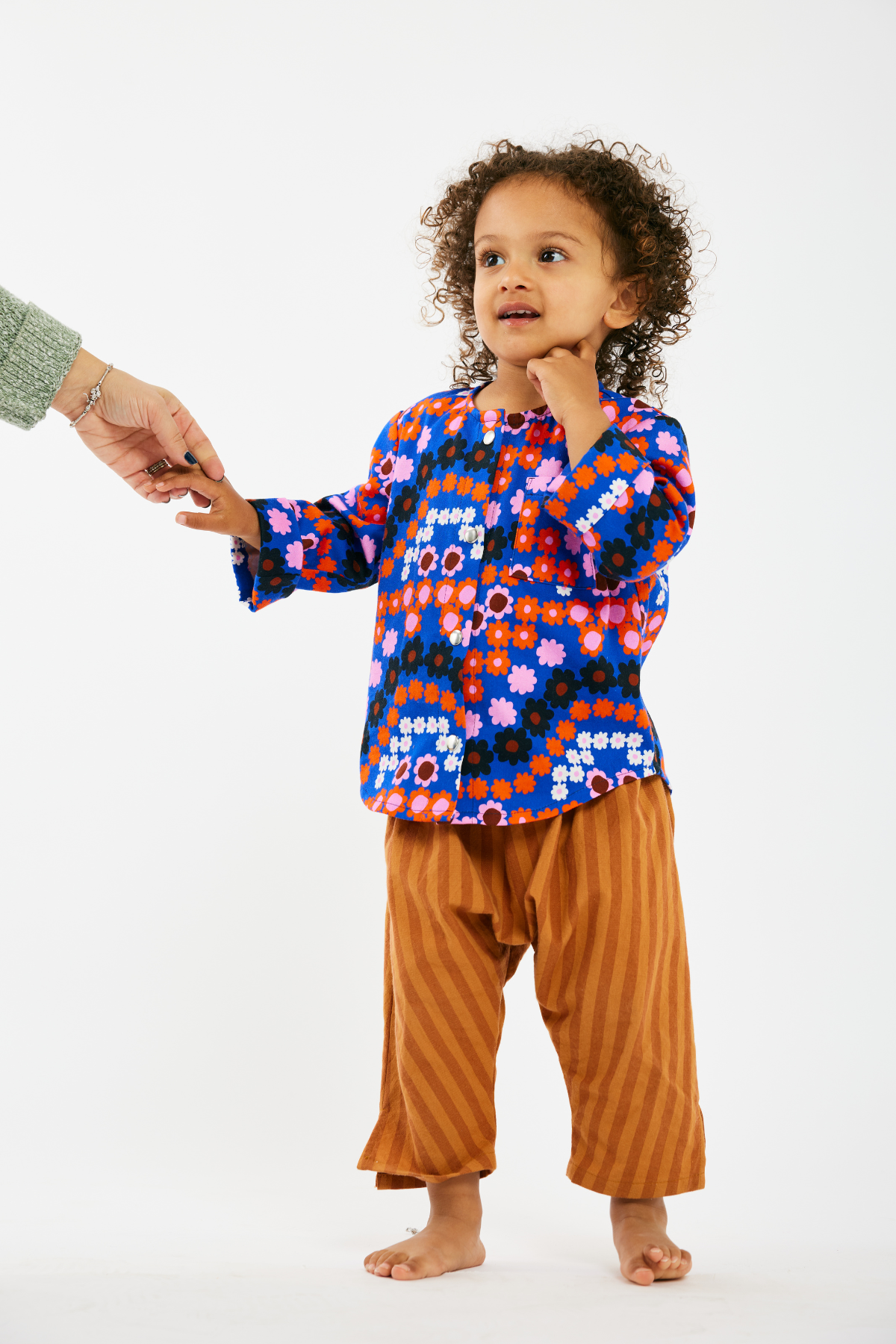 Child wearing a colorful floral shirt by Lilla Barn Clothing and brown stripe pants on a white background