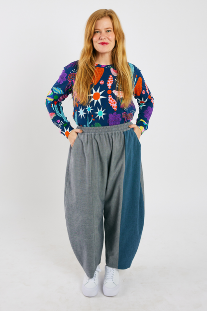 person wearing gray and blue barrel-leg pants made from sustainable bamboo and cotton. She's also wearing a colorful, organic cotton long sleeve t-shirt